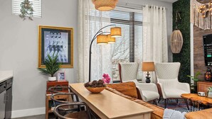 A modern living room with a dining area, featuring a wooden table, chairs, a sofa, and a large framed picture on the wall.