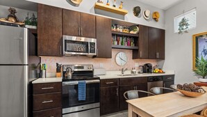 A modern kitchen with dark wood cabinets, stainless steel appliances, a wooden dining table, and a clock on the wall.