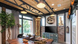 A modern living room with a large wooden dining table, comfortable seating, a TV, and a fireplace. - Industrial Design Apt | 10 Min to Downtown (Nashville)