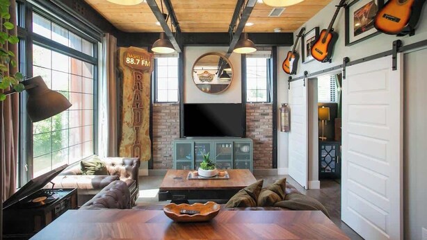 A cozy living room with a large window, a fireplace, and a television. - Industrial Design Apt | 10 Min to Downtown (Nashville)