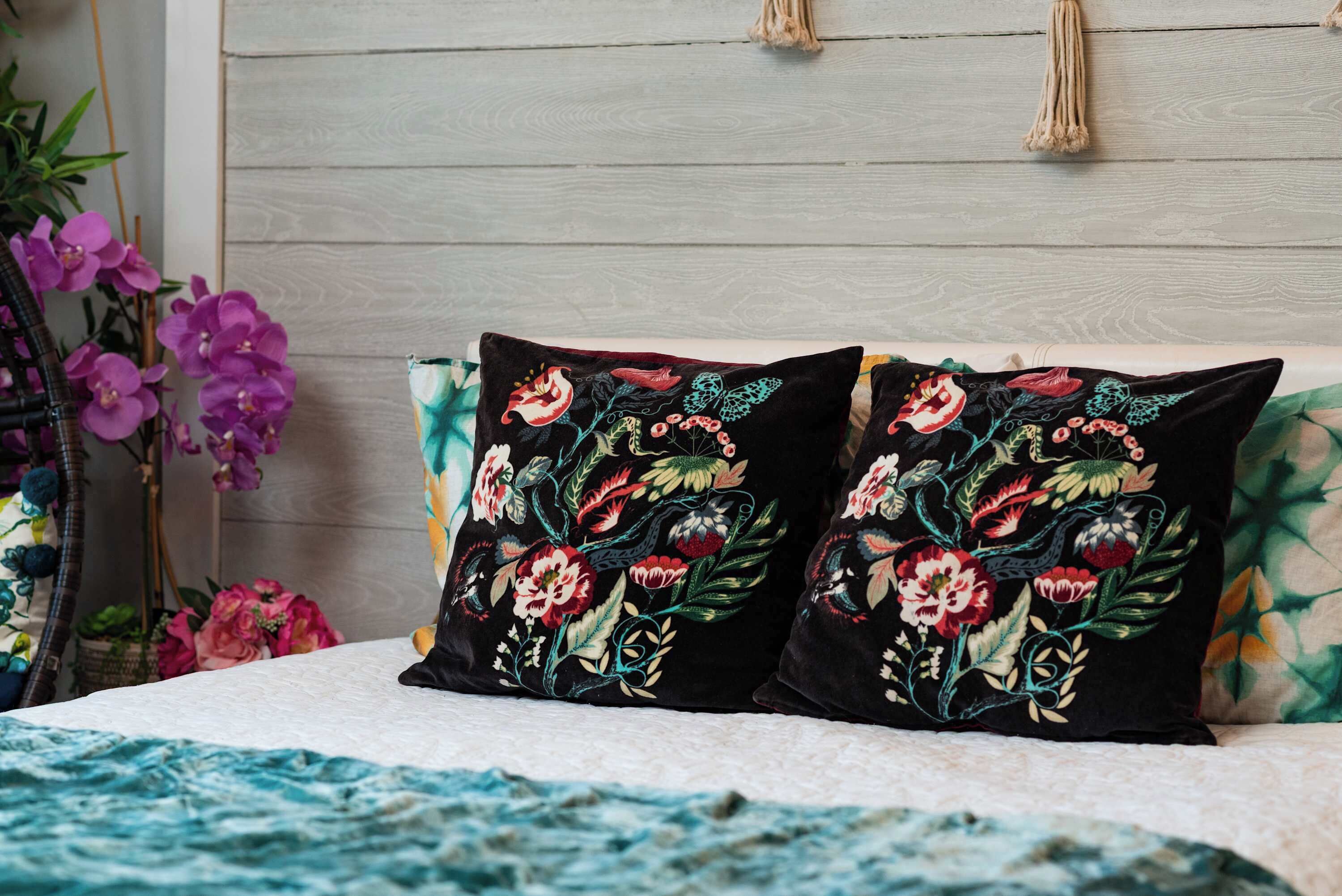 Un letto con due cuscini neri decorati con ricami floreali colorati, una coperta bianca e una testiera in legno.
