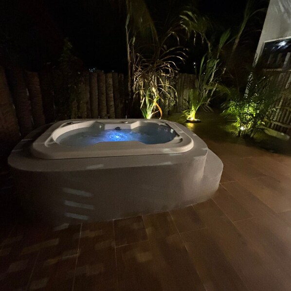Un bain à remous situé dans un espace jardin, avec un sol carrelé et des plantes environnantes.