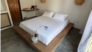 Un lit avec un cadre en bois, une courtepointe blanche matelassée et un seau contenant une bouteille et des verres sur le côté.