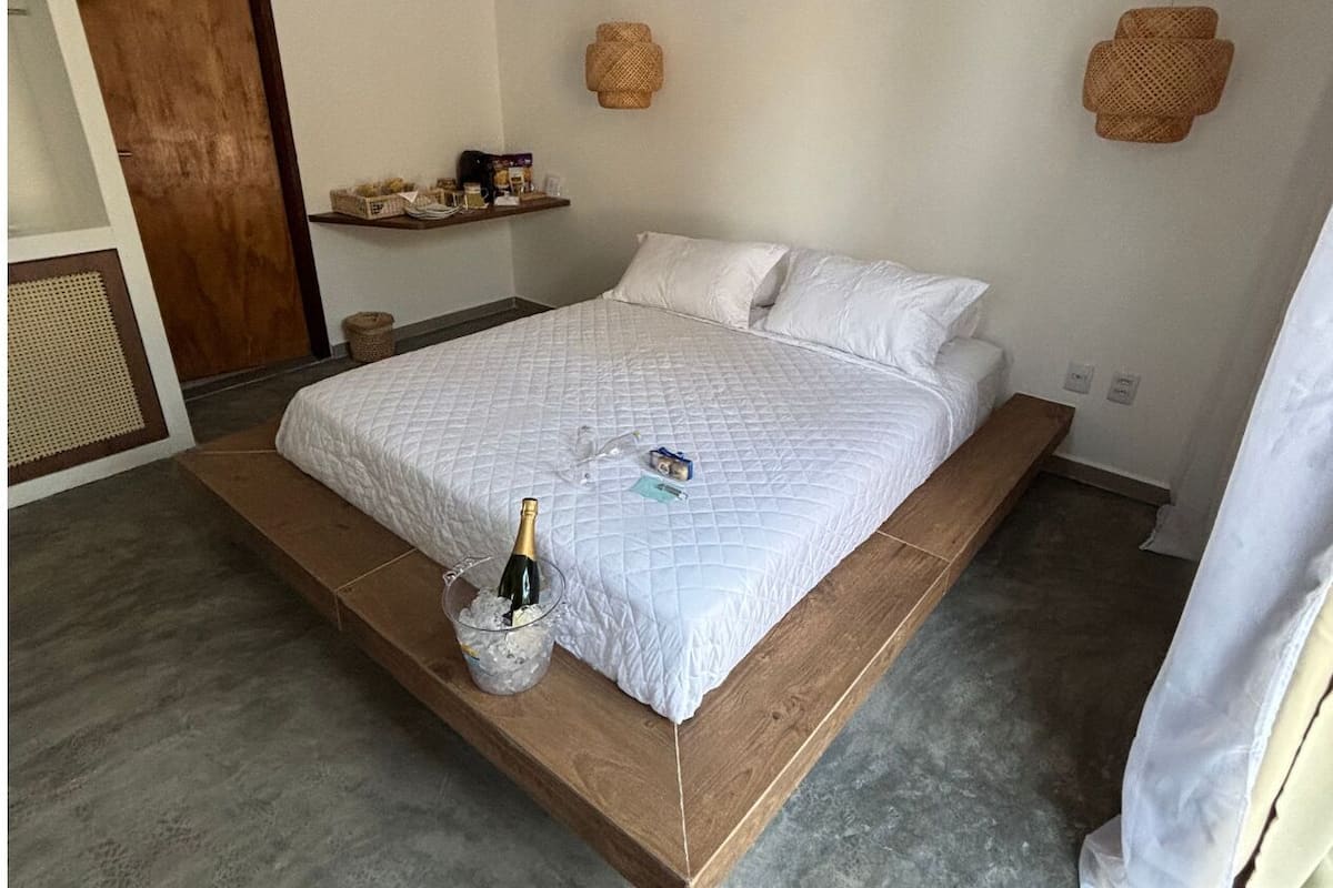 Un lit avec un cadre en bois, une courtepointe blanche matelassée et un seau contenant une bouteille et des verres sur le côté.