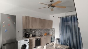 A modern kitchen with a built-in washing machine, a dining table set for four, and a ceiling fan. - Haraki Blue Houses (Rhodes)