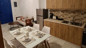 A compact kitchen with wooden cabinets, a refrigerator, a coffee maker, and a toaster. - Haraki Blue Houses (Rhodes)
