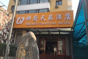 L’entrée d’un hôtel, avec une enseigne indiquant « HÔTEL SHUAIFU TIANYUAN » et une grande pierre portant des inscriptions devant l’entrée.