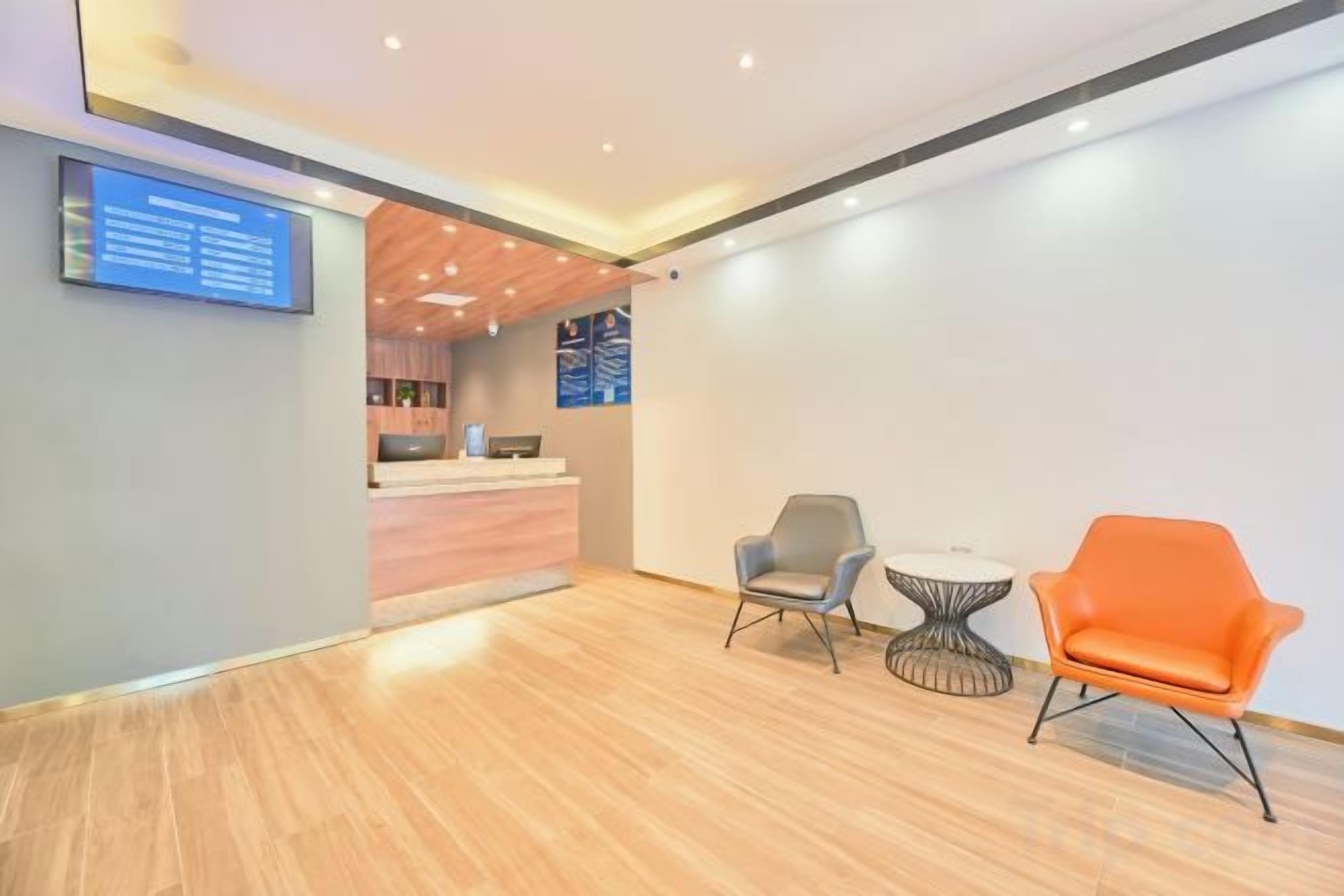 A reception area with a wooden floor, a reception desk, two chairs, and a wall-mounted screen.