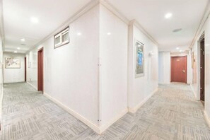 Un couloir d’hôtel avec un tapis à motifs, des murs blancs et des portes donnant sur les chambres.