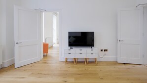 Une pièce avec un meuble TV blanc, un plancher en bois et des portes blanches.