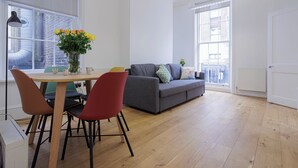 Un salon moderne avec un canapé gris, une table de salle à manger ronde en bois et des chaises rouges, ainsi qu’un vase rempli de fleurs jaunes.