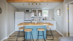 A modern kitchen with a central island, bar stools, and a wooden ceiling. - Charming cottage with Rock View Morro Bay (Morro Bay)