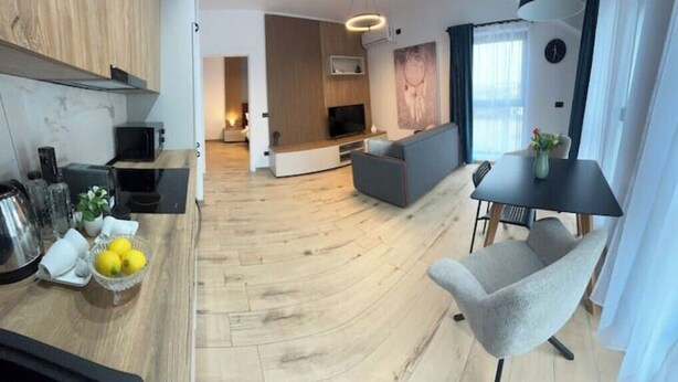 A modern living room with a sofa, a dining table with chairs, and a kitchen area with a microwave and a bowl of lemons.