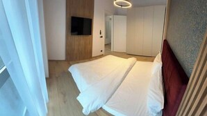 A modern bedroom with a large bed, a flat-screen TV mounted on the wall, and a wooden wardrobe.