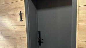 Een donkerdeur met een eenvoudige deurklink, ingebouwd in een houten muur waar het cijfer '1' op staat.