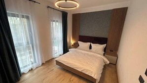 Een moderne slaapkamer met een groot bed, houten vloer en een rond hanglamp erboven.
