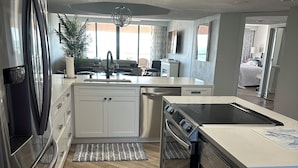 A modern kitchen with stainless steel appliances, a central island, and a view to the living area.