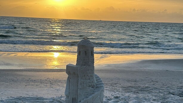 A sandcastle on a beach with the ocean and sunset in the background.