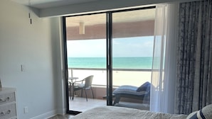 A bedroom with a large bed, a ceiling fan, and a view of the beach through a sliding glass door.