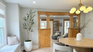 A modern dining area with a wooden table, grey upholstered chairs, and a large potted plant.