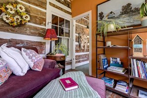 A cozy living room with a purple sofa, a red lamp, a bookshelf, and a painting on the wall.