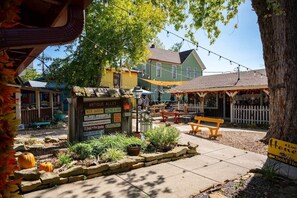Uma área de estar ao ar livre charmosa, com um banco de madeira rústico e uma placa indicando comodidades como um jardim de cerveja e um bistrô.