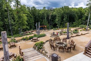 An outdoor seating area with wooden tables and benches, surrounded by a forested landscape.