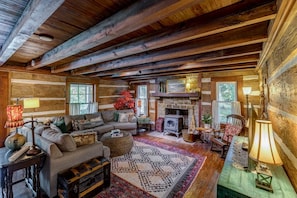 A rustic cabin interior with a wooden ceiling, a fireplace, a sofa, and a dining table.