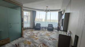 Habitación de hotel con una cama grande, un escritorio, dos sillas, un televisor y vista a la ciudad.