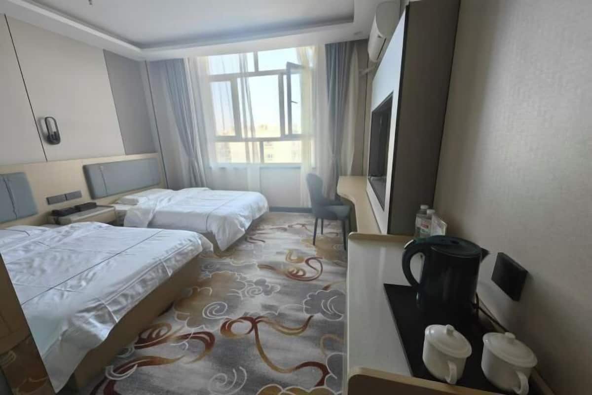 Une chambre d’hôtel avec deux lits, un bureau avec une machine à café, une télévision et une fenêtre avec des rideaux.