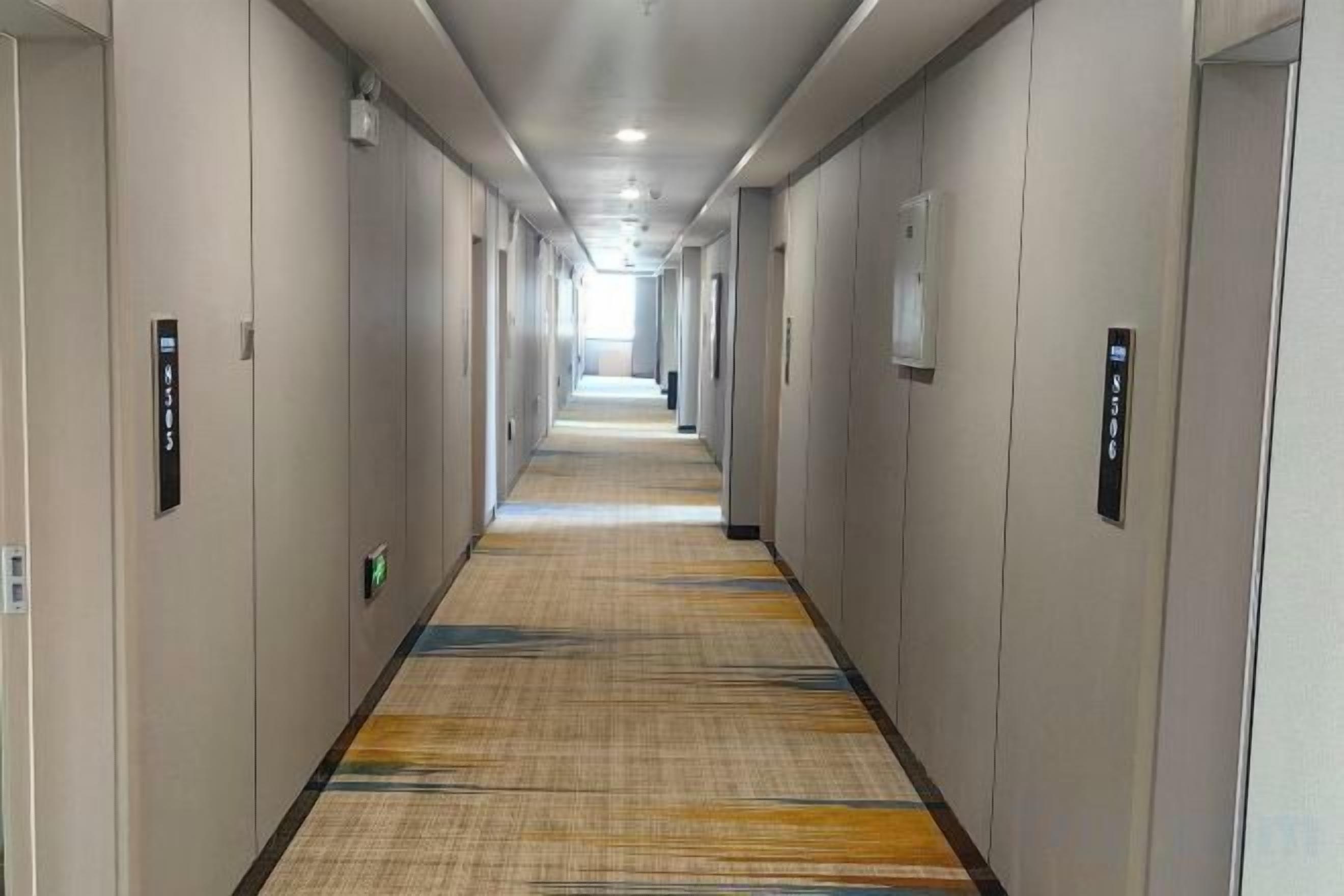 Een hotelgang met deuren aan beide kanten, een vloerbedekking en een lange gang die naar een helder einde leidt.