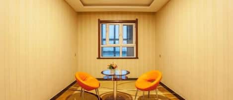 A hotel room with a large window, two orange chairs, and a small round table.
