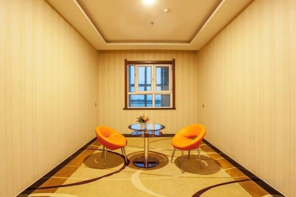 Una habitación de hotel con un ventanal grande, dos sillas naranjas y una pequeña mesa redonda.