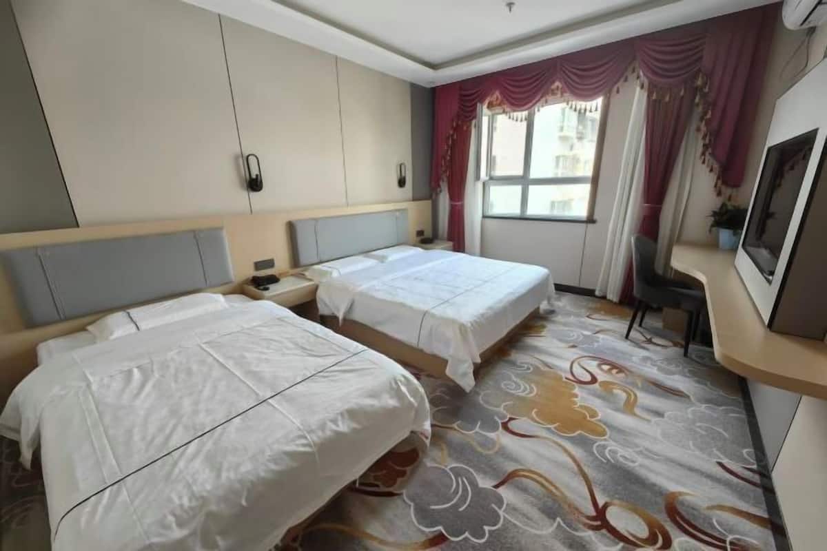 Une chambre d’hôtel avec deux lits, un bureau, une chaise et une fenêtre avec des rideaux.