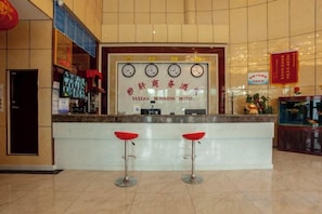 Una zona de recepción con un mostrador, dos taburetes rojos y un reloj sobre el mostrador.