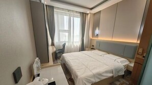 Habitación de hotel con cama, mesita de noche, silla, escritorio y ventana con cortinas.