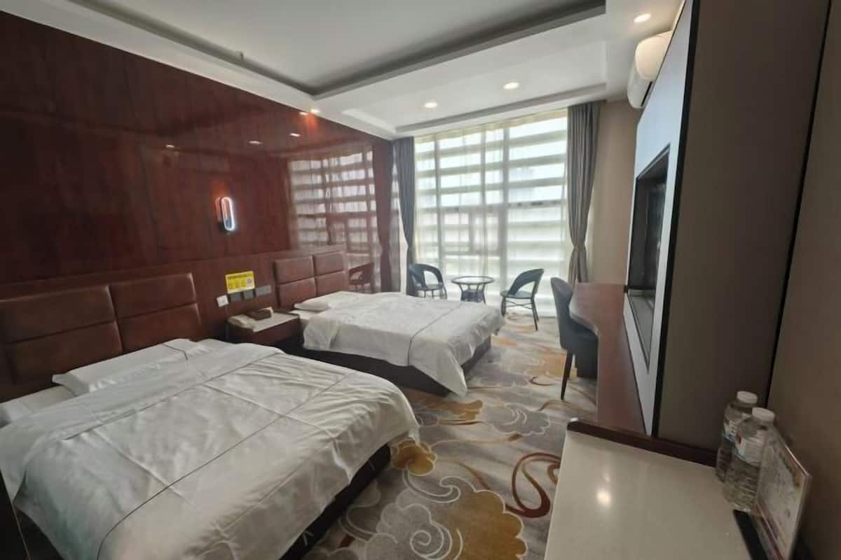 Une chambre d’hôtel avec deux lits, une télévision, une petite table et une fenêtre avec des rideaux.