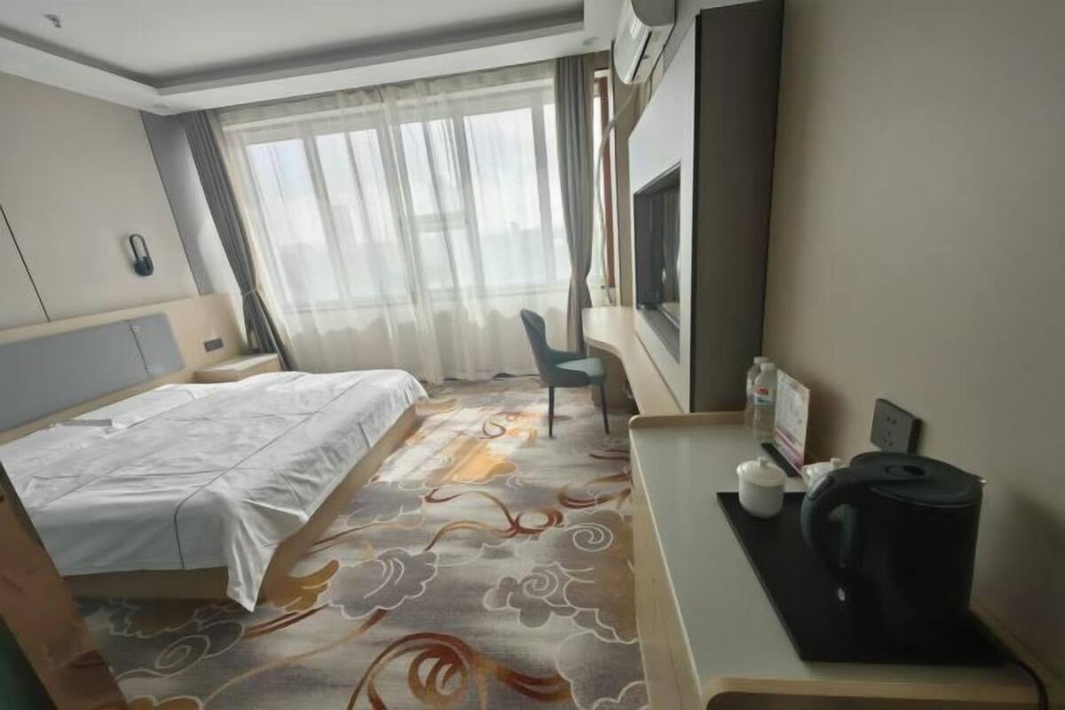 Une chambre d’hôtel comprenant un lit, un bureau avec une bouilloire, une chaise, une télévision et une fenêtre avec des rideaux.