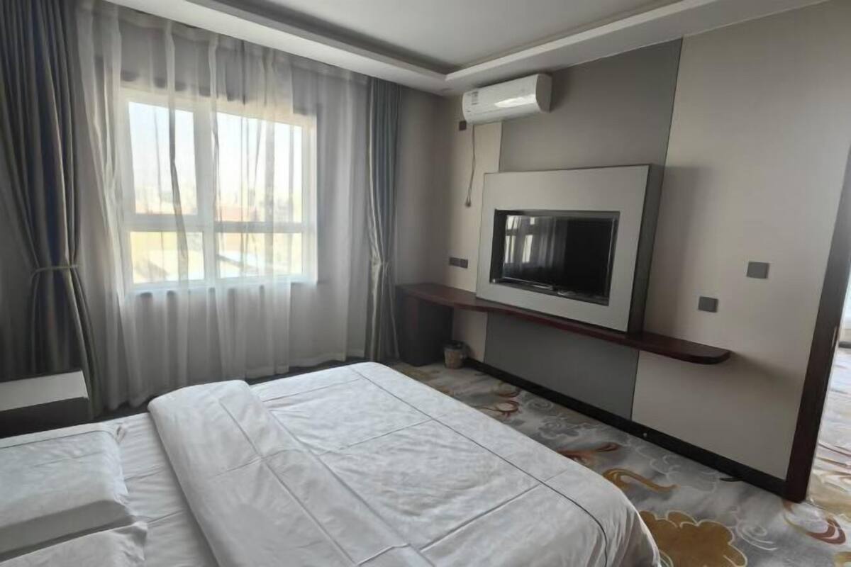 Une chambre d’hôtel avec un lit, un téléviseur fixé au mur et une fenêtre avec des rideaux.