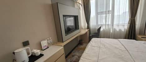 Une chambre d’hôtel équipée d’un lit, d’un téléviseur fixé au mur, d’une machine à café et d’une petite table avec des tasses et un menu.