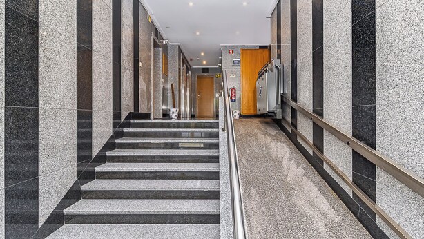 A modern hotel corridor with marble walls, a metal railing, and a staircase leading to a wooden door. - Stylish Stay in Lisbon-Scenic Views (Lisbon)