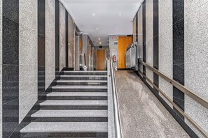 En moderne hotelgang med marmorvægge, gelænder i metal og en trappe, der fører op til en trædør.