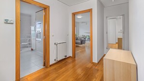 A hallway with wooden flooring, white walls, and a radiator. There is a door leading to a kitchen area with a refrigerator and a microwave. - Stylish Stay in Lisbon-Scenic Views (Lisbon)