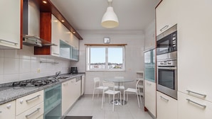 A modern kitchen with white cabinets, a gas stove, an oven, and a dining area with a round table and chairs. - Stylish Stay in Lisbon-Scenic Views (Lisbon)