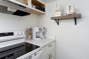 A modern kitchen with a built-in oven, a coffee maker, and a shelf with utensils.