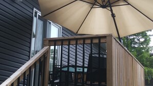 A wooden deck with a large beige umbrella, a wooden railing, and a table with chairs. - Relax and enjoy your home away from home. (Strathroy)