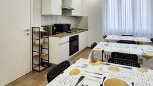 A modern kitchen with white cabinets, a microwave, and a sink. There are dining tables with white tablecloths and black chairs.