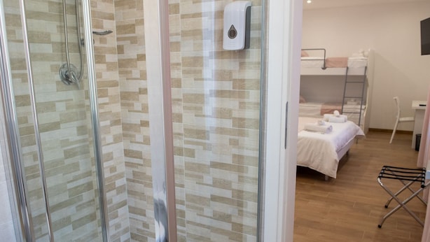 A hotel room with a shower, a bed, a bedside table, and a drying rack.