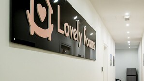A sign for 'Lovely Rooms' with a heart symbol, a door, and a refrigerator in a hallway.