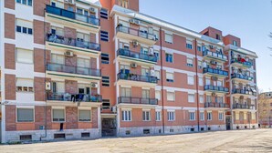 A multi-story residential building with balconies, air conditioning units, and a parking lot in front. - Lovely Rooms - Room 3 by Rentbeat (Civitavecchia)